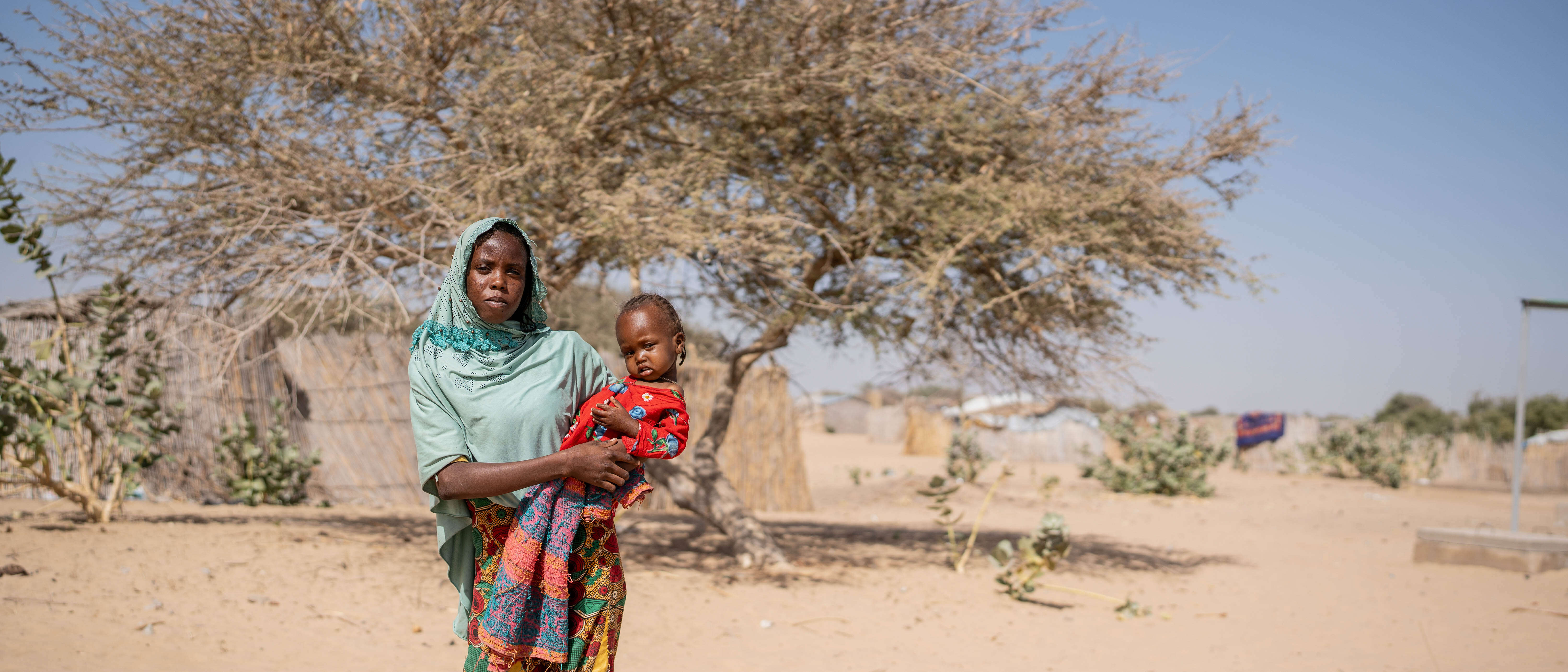 A mother holds her child on her hip in front of a barren back drop.