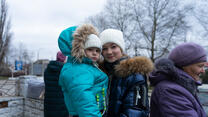 Young girl stands, carrying her baby sister, both facing the camera.