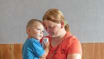 A mother holds her young son in her arms, looking down and smiling at him.